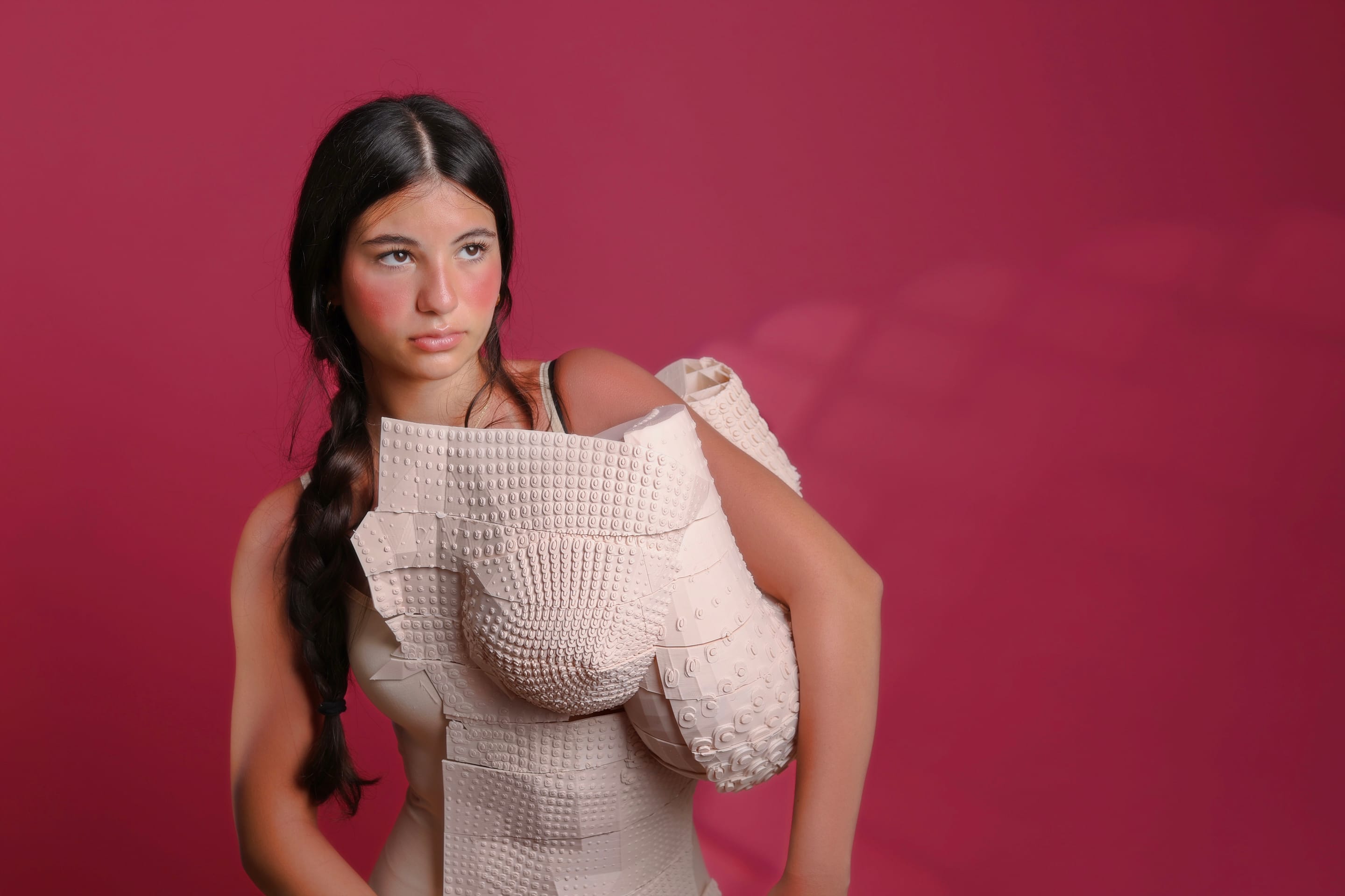 Waist-up shot of the model with a long braid looking aside in the asymmetric textured nude corset against a magenta backdrop