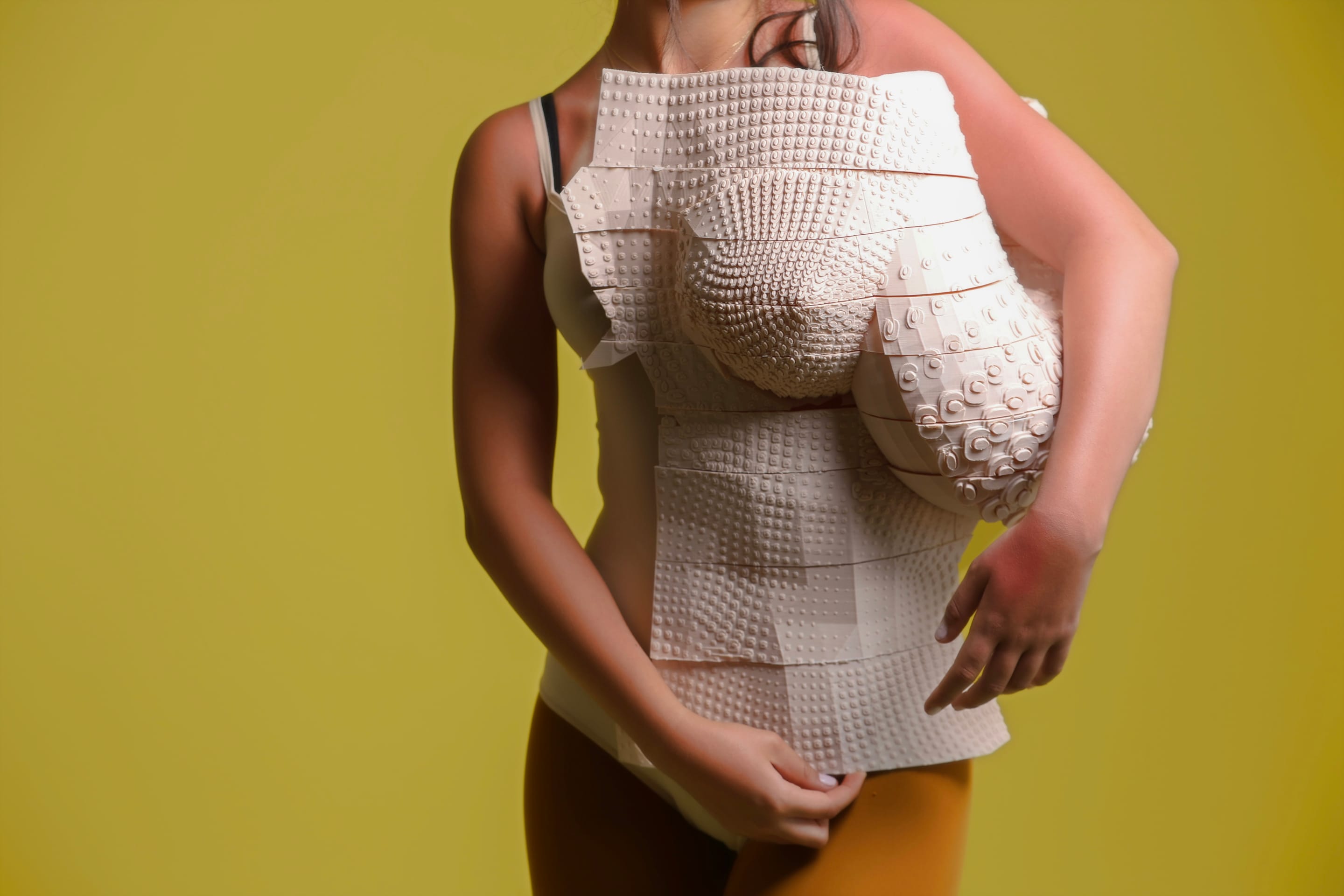 Torso shot of the textured corset with sculpted bust panel over a bodysuit and mustard tights, face out of frame, olive-yellow backdrop