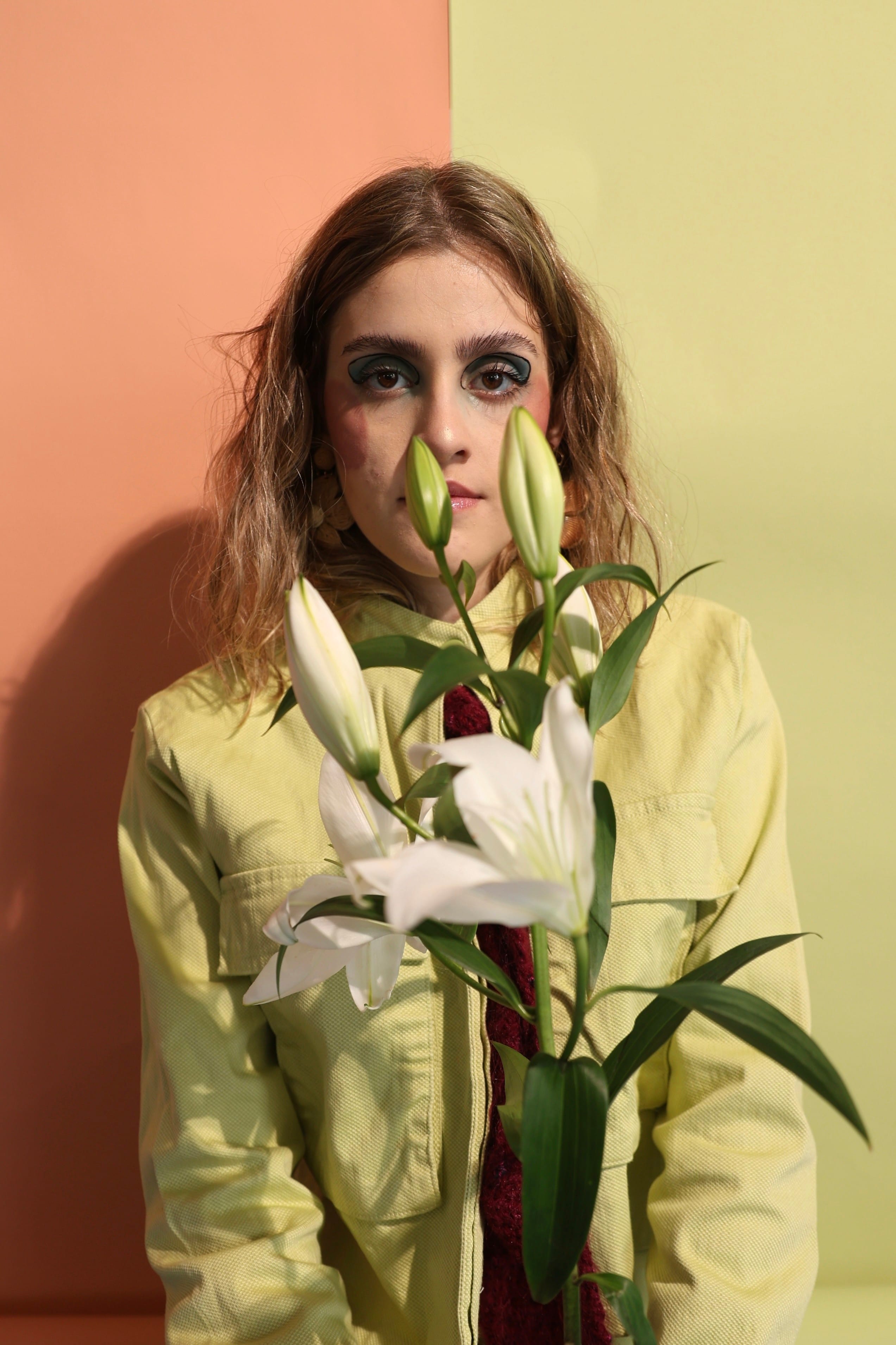 Front-facing portrait of a model in a lime-green jacket and burgundy tie, white lilies in the foreground partly covering the lower face