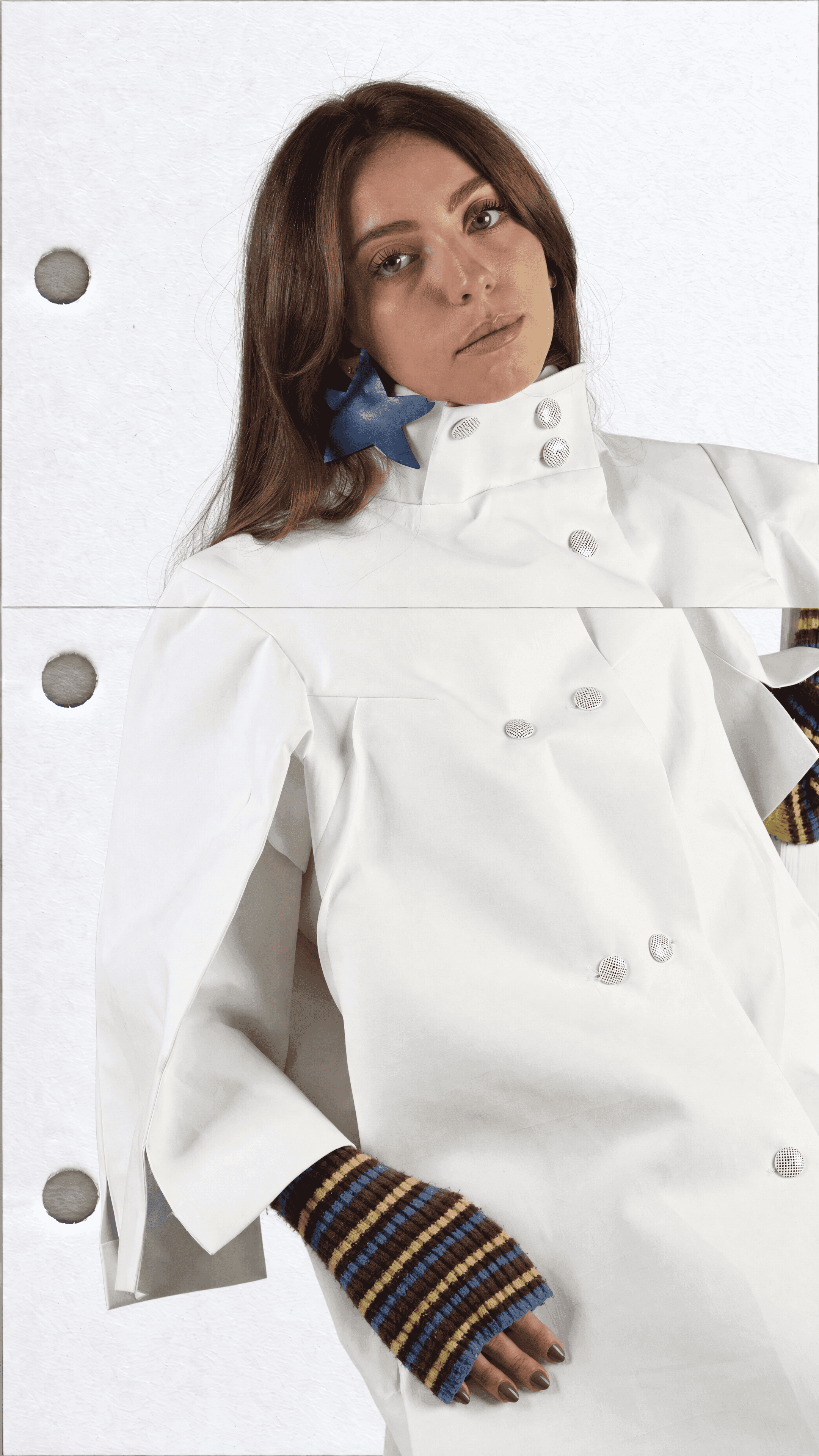 Close-up of a model in a white double-breasted coat with a high buttoned collar, a blue star earring and striped fingerless gloves