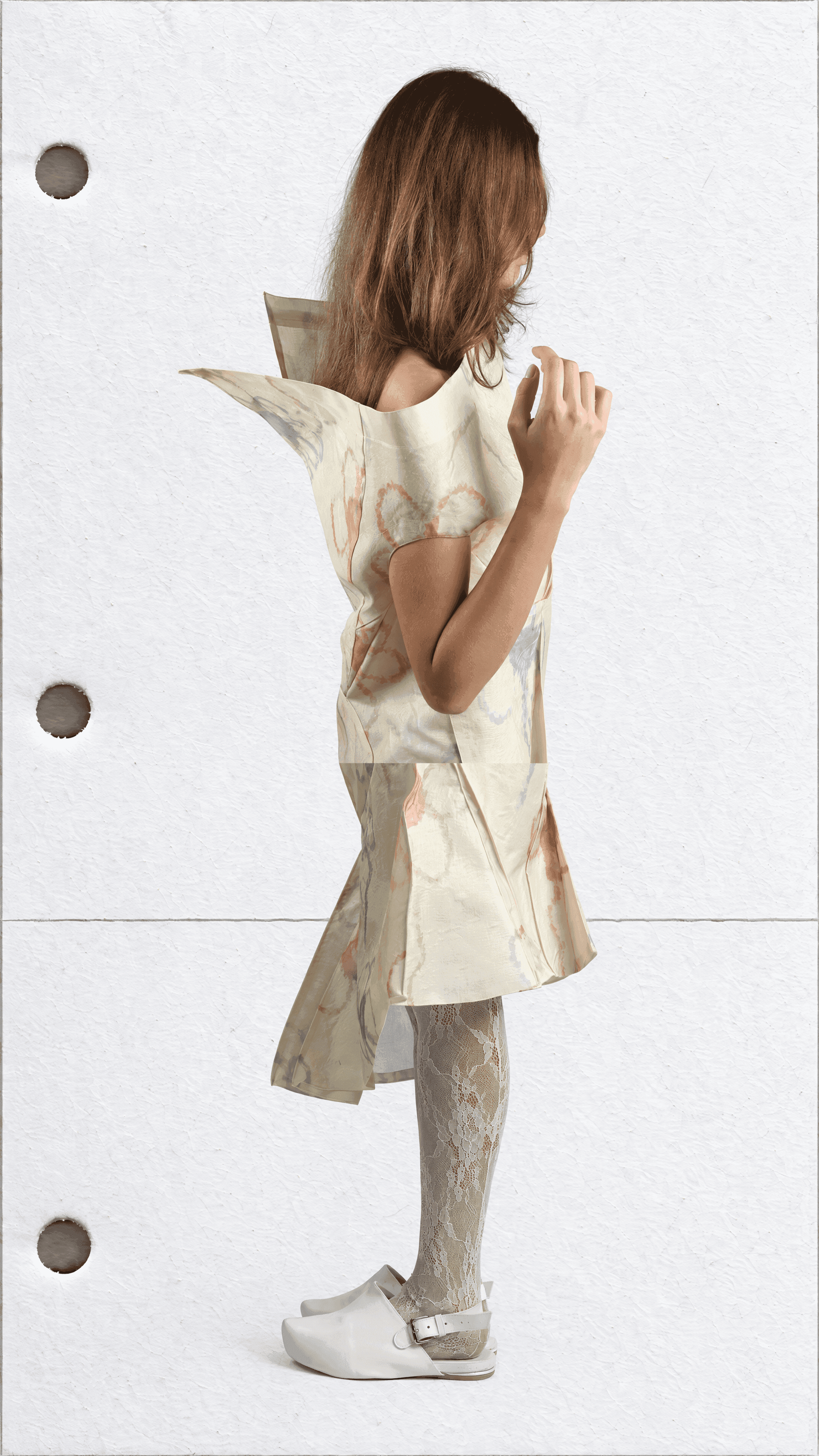 Full-length side-back view of a model turned away, hand at shoulder, in a cream flower-print dress with a pointed shoulder panel and draped skirt