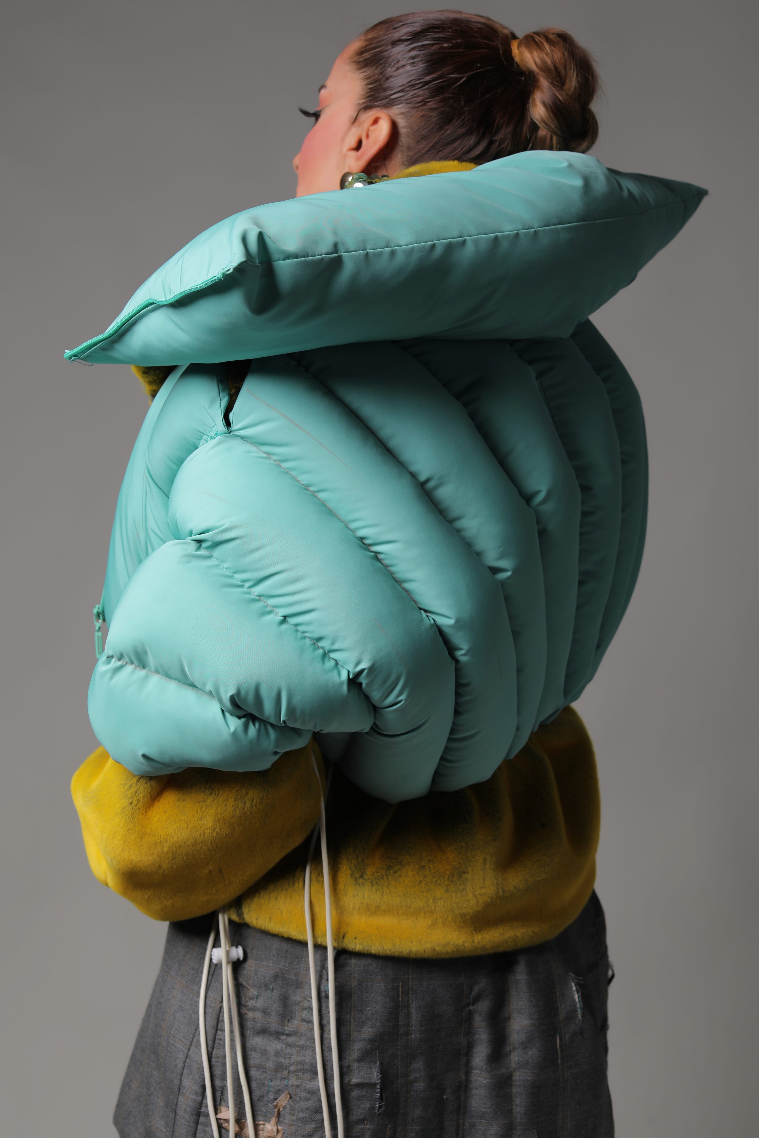 Back view of a cropped mint puffer with channel-quilted padding and a pillow-like collar over yellow plush and grey suiting