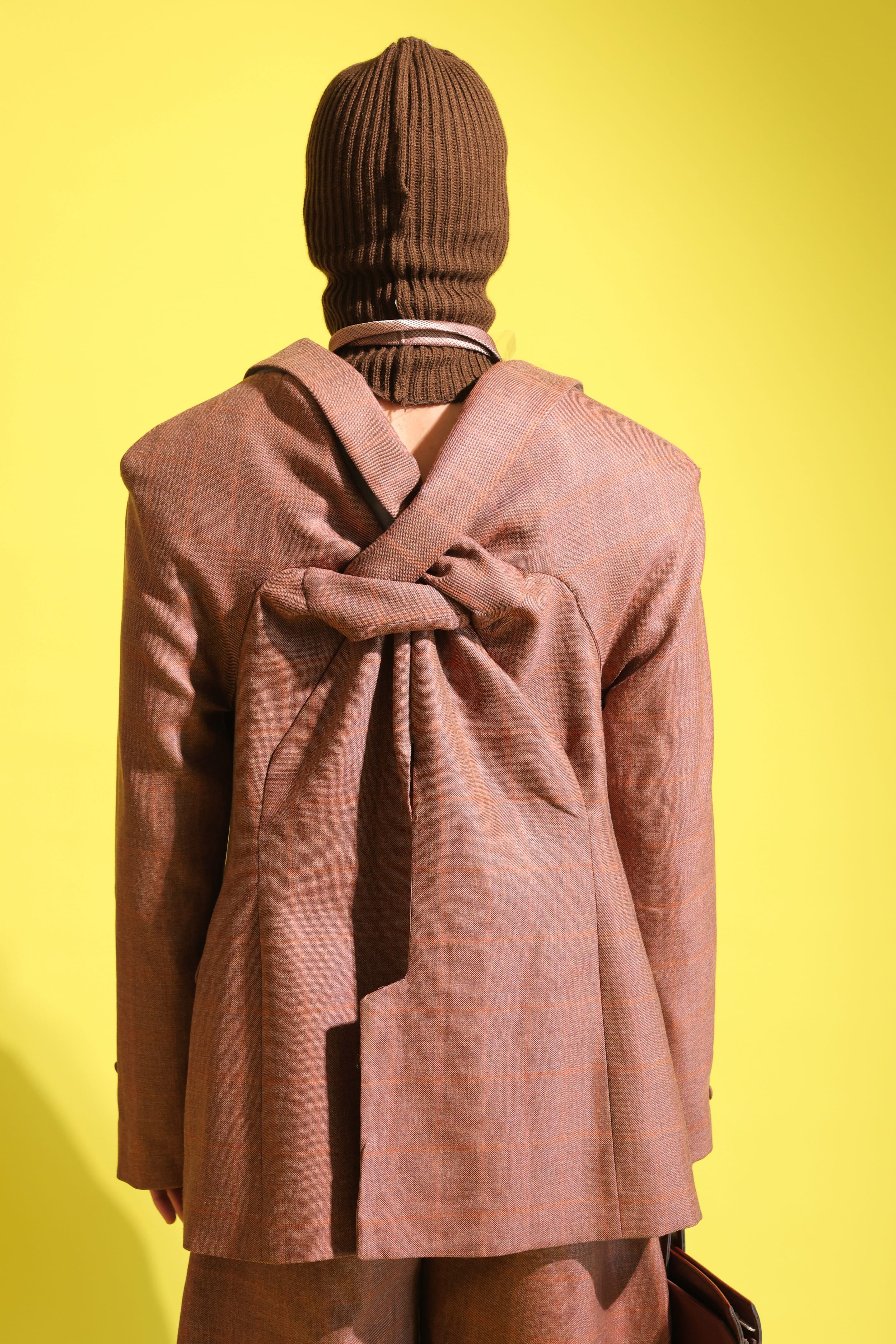Close back view of the rust check blazer, fabric twisted into a looped knot between the shoulder blades, brown balaclava above
