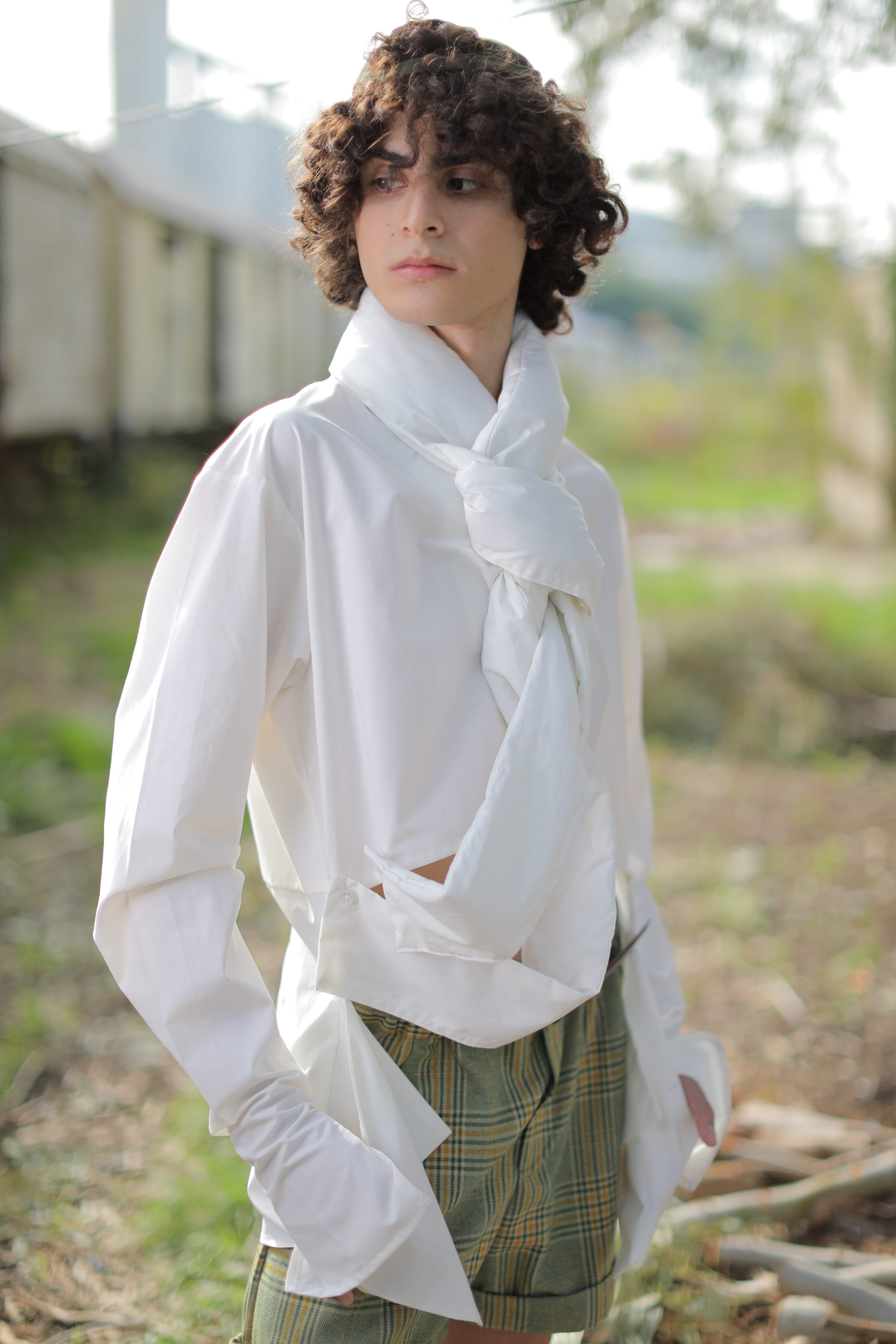 Thigh-up portrait of the model looking aside, the white shirt's collar twisted into a long knot that drapes across the chest